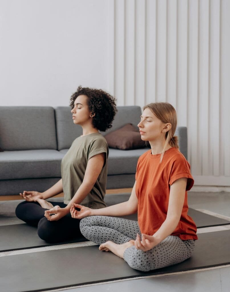 duas mulheres meditando em casa, umas das modalidades esportivas que promovem o bem-estar