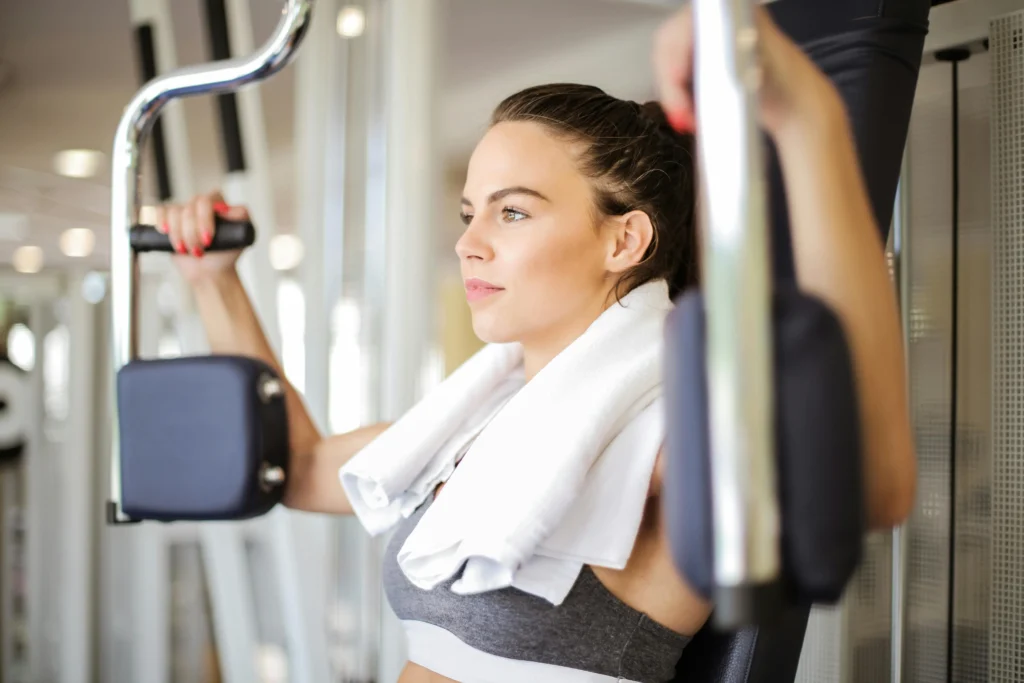 Mulher concentrada treinando bíceps na academia com toalha no pescoço, simbolizando foco e os benefícios mentais da musculação.