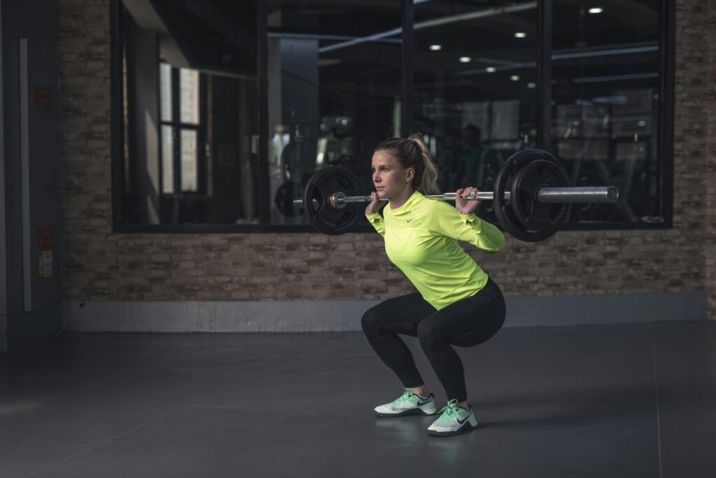Mulher treinando agachamento livre com barra na academia, exercício fundamental na musculação para mulheres focada em glúteos e pernas.