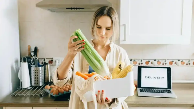 Mulher pensativa organizando alimentos frescos na cozinha, refletindo sobre a comida e escolhas saudáveis.
