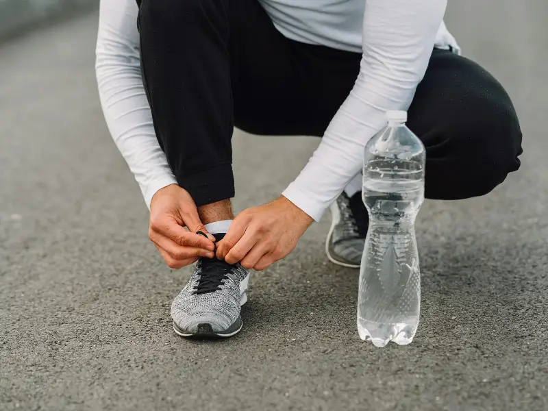 Homem se preparando para treinar, amarrando o tênis — representando o início da disciplina no treino.