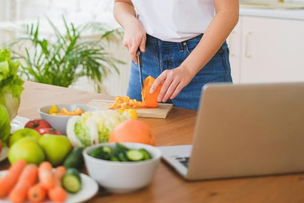 Card com imagem de mulher na cozinha cortando alimento na tábua, representando a categoria nutrição e bem-estar do tema em foco.